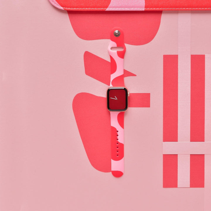 A Coconut Lane smartwatch, adorned with the Abstract Pink & Red Apple Watch Strap, is showcased against a pink and red abstract background. The watch face is square with a red display, featuring a minimalistic white line design.