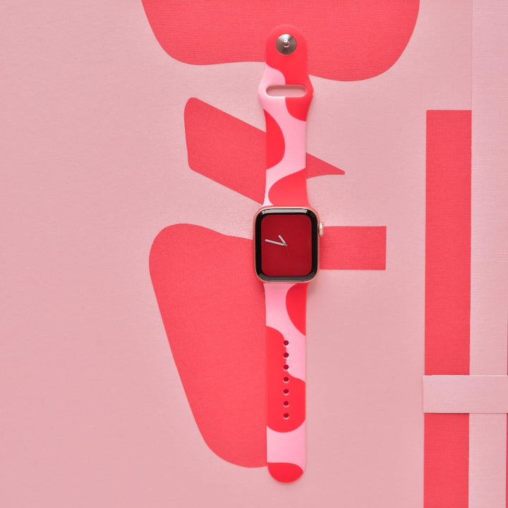 A smartwatch featuring the Abstract Pink & Red Apple Watch Strap from Coconut Lane is showcased against a corresponding abstract backdrop. The watch face, adorned in red with a minimalistic single white hand, perfectly harmonizes with the striking design of the strap and its vivid background.